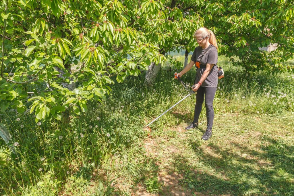 A woman mows grass on his property with a Gas-Powered Weed Wacker A woman mows grass on his property with a Gas-Powered Weed Wacker