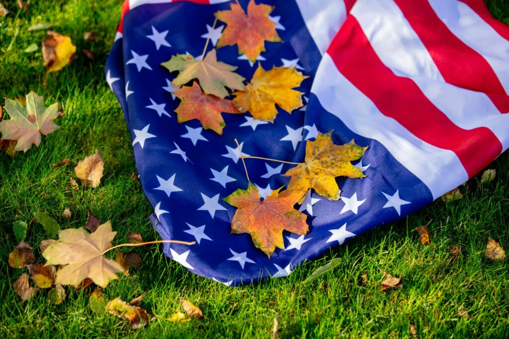 American flag with maple leaves on green grass in autumn