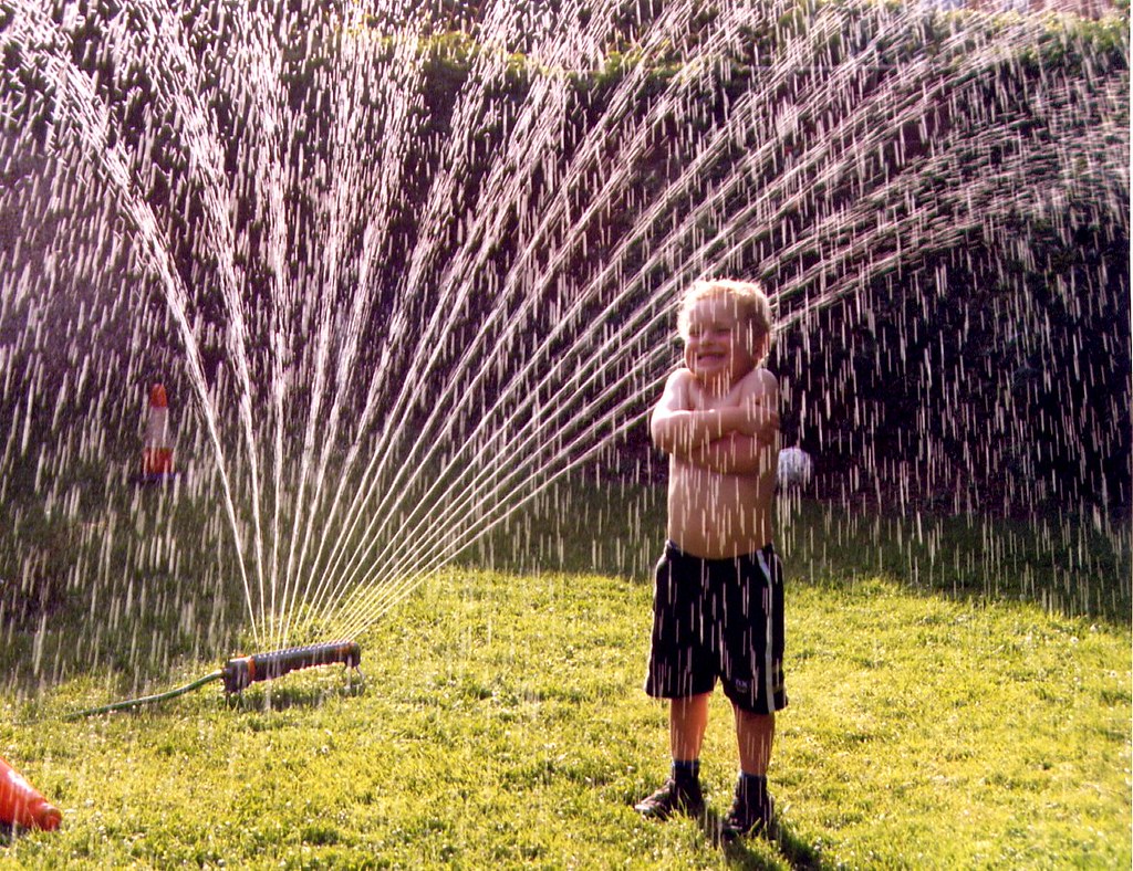 Young child standing in the middle of a garden sprinkler.