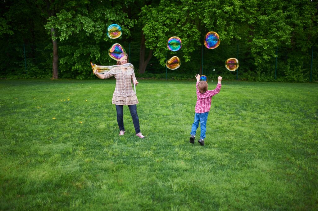 Mom and children playing soap bubbles on the green lawn in the park.