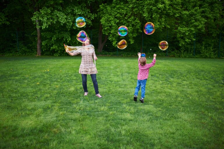 Mom and children playing soap bubbles on the green lawn in the park.