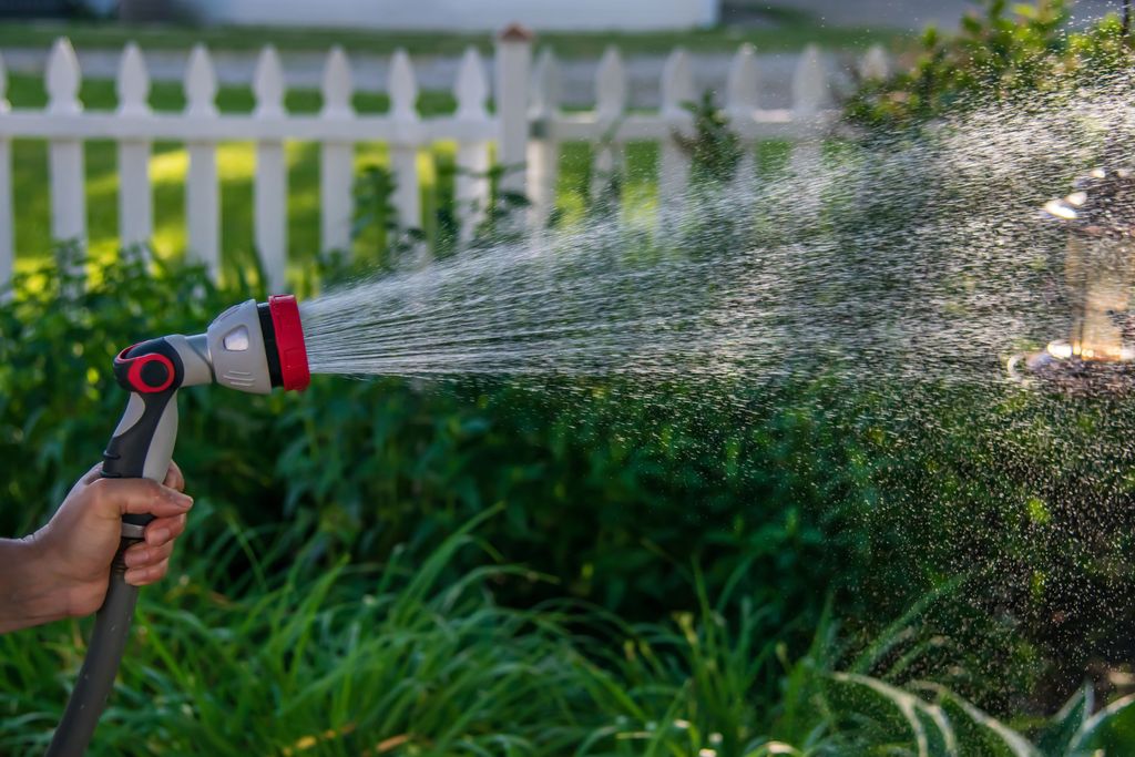 A person spraying water onto plants in a garden with a spray nozzle.