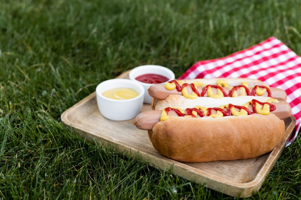 4th of July - wooden tray with sauce bowls and hot dogs near checkered table napkin on green lawn 4th of July - wooden tray with sauce bowls and hot dogs near checkered table napkin on green lawn